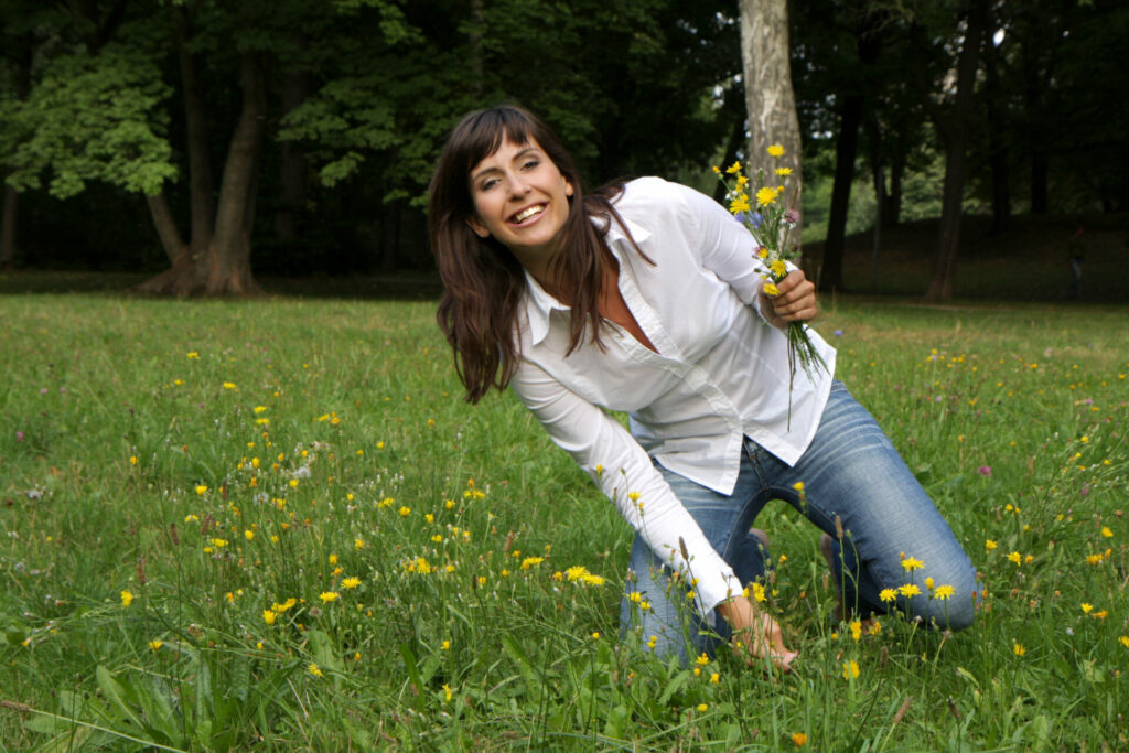 Woman crouching in grassy park holding yellow flowers and smiling at camera