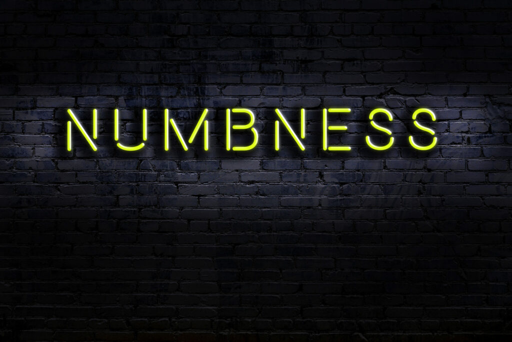 Yellow neon sign reading NUMBNESS on dark brick wall