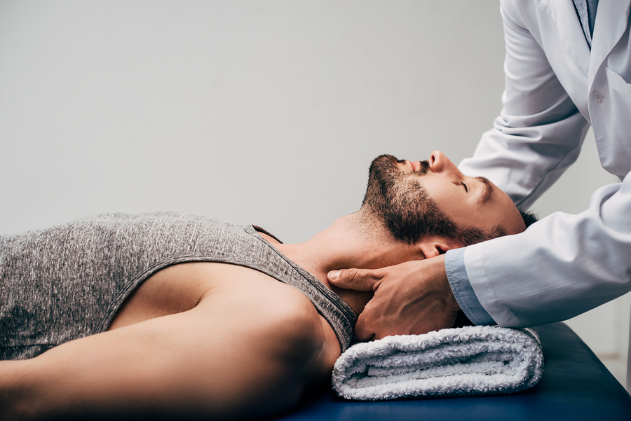 Chiropractor performing neck massage and manipulation on male patient lying face up on treatment table