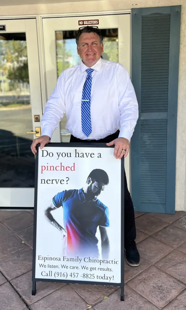 Dr. Espinosa at the office door beside a sidewalk sign that asks, Do you have a pinched nerve?