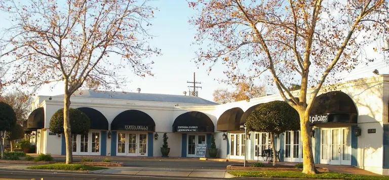 The single-storey building at 3330 Folsom Blvd: white arches and dark awnings under bare winter trees